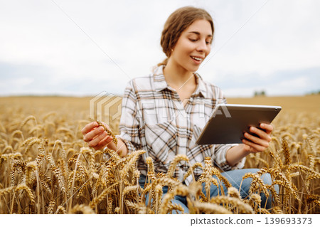 Woman agronomist in a field with a tablet checks the growth of the crop. New harvest concept. Woman agronomist in a field with a tablet checks the growth of the crop. New harvest concept. 139693373
