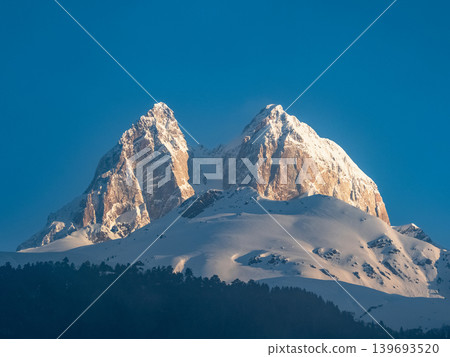 Mount Ushba in Svaneti, Georgia. Snow-capped peaks rise sharply against a clear blue sky Mount Ushba in Svaneti, Georgia. Snow-capped peaks rise sharply against a clear blue sky 139693520
