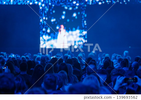 Audience watching live stage performance on large screen at blue light event Audience watching live stage performance on large screen at blue light event 139693562