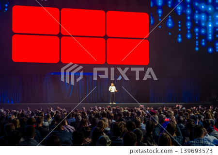 Keynote speaker on stage presenting to large audience at conference with vibrant LED screens Keynote speaker on stage presenting to large audience at conference with vibrant LED screens 139693573