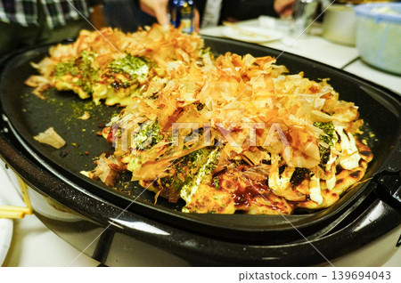 Sprinkle bonito flakes on the okonomiyaki once it's cooked. 139694043