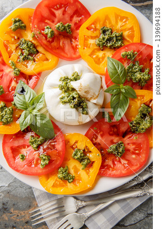 Burrata cheese appetizer with fresh tomatoes, basil pesto and balsamic vinegar close-up in a plate on the table. Vertical top view Burrata cheese appetizer with fresh tomatoes, basil pesto and balsamic vinegar close-up in a plate on the table. Vertical top view 139694188