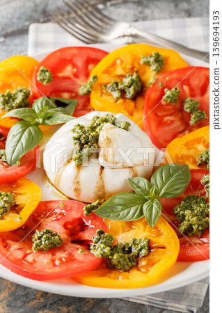 burrata caprese salad with multi-colored tomato and basil pesto closeup on the plate. Vertical burrata caprese salad with multi-colored tomato and basil pesto closeup on the plate. Vertical 139694193