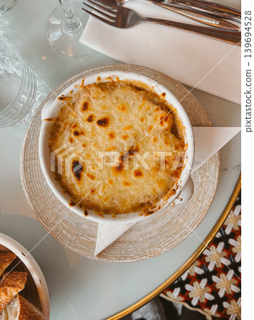 French onion soup with melted golden cheese served in a Paris cafe, classic comfort food in a ceramic bowl with warm restaurant atmosphere 139694528