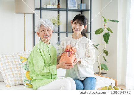 A middle-aged daughter gives a gift to her senior mother. A middle-aged daughter gives a gift to her senior mother. 139694772