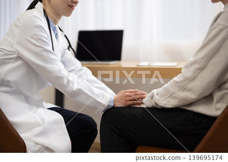 A close-up of the hands of a female doctor in a white coat as she holds a patient's hand. A close-up of the hands of a female doctor in a white coat as she holds a patient's hand. 139695174