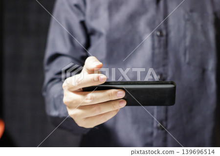 Man holding a black rectangular device in his hand. Playing a Video with Gadget. Business and Technology Concept. High quality photo 139696514