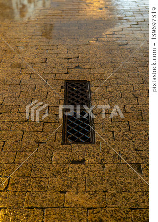 Wet Cobblestone Street With Metal Drain Grate at Night Reflective Urban Pavement Texture Wet Cobblestone Street With Metal Drain Grate at Night Reflective Urban Pavement Texture 139697319
