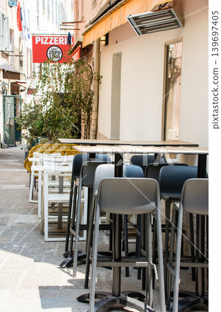 Chairs and tables lined up in front of a shop under the bright sunlight in Ajaccio, Corsica, known for its Napoleon fabrics. 139697405