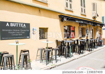 Chairs and tables lined up in front of a shop under the bright sunlight in Ajaccio, Corsica, known for its Napoleon fabrics. Chairs and tables lined up in front of a shop under the bright sunlight in Ajaccio, Corsica, known for its Napoleon fabrics. 139697409