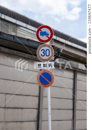 Road signs and a speed limit sign of 30 in front of a concrete block wall. Road signs and a speed limit sign of 30 in front of a concrete block wall. 139697477