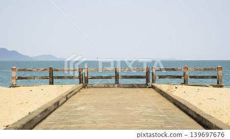 Minimalist seaside scene in Vietnam with a concrete pier leading to the ocean, calm blue water, and distant islands under a clear sky. Minimalist seaside scene in Vietnam with a concrete pier leading to the ocean, calm blue water, and distant islands under a clear sky. 139697676