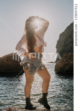 Woman sunset coastline young lady in linen shirt and denim shorts posing on rocky beach during golden hour Woman sunset coastline young lady in linen shirt and denim shorts posing on rocky beach during golden hour 139697812