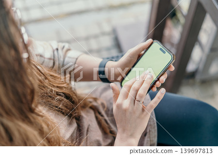 Smartphone mockup woman uses mobile device with green screen for content placement while sitting in outdoor environment Smartphone mockup woman uses mobile device with green screen for content placement while sitting in outdoor environment 139697813