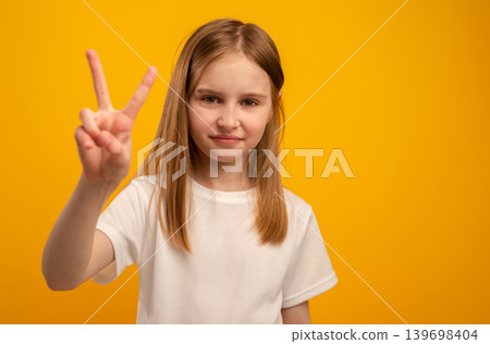 Adorable Girl Flashes A Victory Sign With Fingers Against A Vibrant Orange Background 139698404