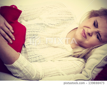 Woman feeling stomach cramps lying on cofa Woman feeling stomach cramps lying on cofa 139698473