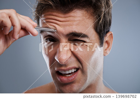 Plucking, eyebrow and portrait of man with tweezers, hair removal and pain in grey background of studio. Beauty, epilation and person with grooming routine and treatment for self care with tools 139698702