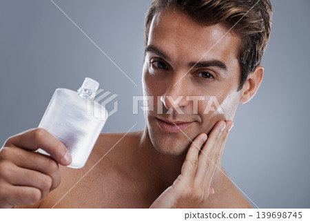 Studio, portrait and man with aftershave for beauty, grooming and facial treatment or cologne. Model, face and happy with bottle for cosmetics product, fragrance and male skincare by gray background Studio, portrait and man with aftershave for beauty, grooming and facial treatment or cologne. Model, face and happy with bottle for cosmetics product, fragrance and male skincare by gray background 139698745