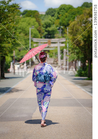 A woman in a yukata (summer kimono) walking towards a shrine gate, holding a red Japanese umbrella, in the castle town of Inuyama. Aichi Prefecture, Japan. A woman in a yukata (summer kimono) walking towards a shrine gate, holding a red Japanese umbrella, in the castle town of Inuyama. Aichi Prefecture, Japan. 139698758