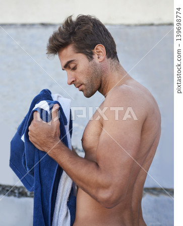 Towel, fitness and young man by wall for outdoor health, wellness or body exercise. Sports, serious and profile of handsome male person with training or workout routine for confidence in summer. 139698774