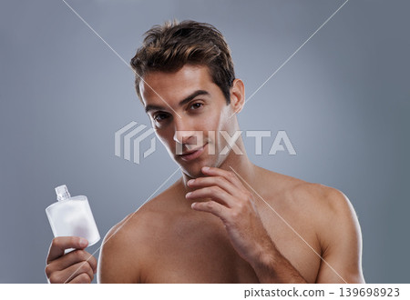 Studio, portrait and man with aftershave for skincare, grooming and facial treatment or cologne. Model, face and happy with bottle for cosmetics product, fragrance and male beauty by gray background 139698923