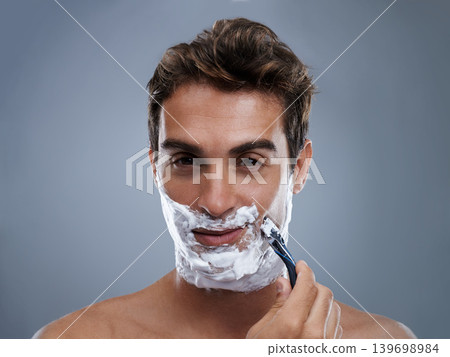Man, razor and shaving beard in studio portrait for grooming, skincare and wellness by grey background. Person, model and blade with cream, facial hair removal and foam product for cosmetic change Man, razor and shaving beard in studio portrait for grooming, skincare and wellness by grey background. Person, model and blade with cream, facial hair removal and foam product for cosmetic change 139698984