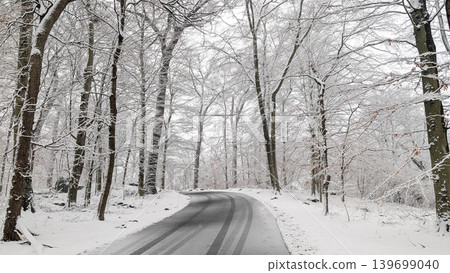 Winding winter road with tire tracks through beautiful snow-covered forest. Winding winter road with tire tracks through beautiful snow-covered forest. 139699040