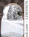 Snowy winter landscape framed by stone archway of a building. 139699076