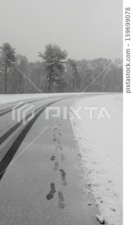 Human footprints and tire tracks on wet asphalt road during winter snowfall. Human footprints and tire tracks on wet asphalt road during winter snowfall. 139699078