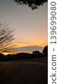 Winding asphalt park path under vibrant orange sunset sky with tree silhouettes. 139699080