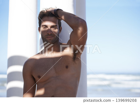 Smile, shirtless and portrait of man outdoor by pillars at beach with confidence on vacation. Happy, model and handsome young male person by wall at ocean or sea for holiday or weekend trip. Smile, shirtless and portrait of man outdoor by pillars at beach with confidence on vacation. Happy, model and handsome young male person by wall at ocean or sea for holiday or weekend trip. 139699208