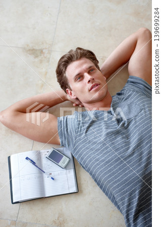 Thinking, floor and above of man with notebook and hands on head for resting, learning and writing in home. Studying, education and face of person on ground with book, cellphone and notes on weekend Thinking, floor and above of man with notebook and hands on head for resting, learning and writing in home. Studying, education and face of person on ground with book, cellphone and notes on weekend 139699284