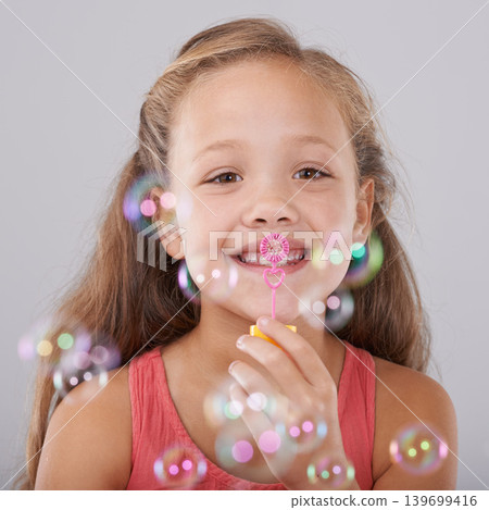 Portrait, kid and blowing bubbles in studio by toy, happiness and fun games for hand eye coordination. Little girl, face and learning to play on soap wand, development and sweet by gray background Portrait, kid and blowing bubbles in studio by toy, happiness and fun games for hand eye coordination. Little girl, face and learning to play on soap wand, development and sweet by gray background 139699416