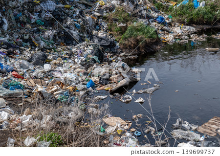 Plastic waste and trash cover the banks of a river in a polluted area, demonstrating environmental damage and neglect 139699737