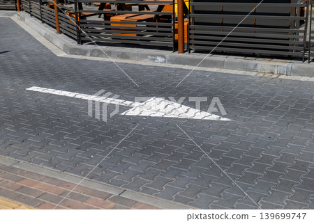 A clear marking on the ground points cars in a specific direction at a parking area close to tables and chairs for outdoor use A clear marking on the ground points cars in a specific direction at a parking area close to tables and chairs for outdoor use 139699747