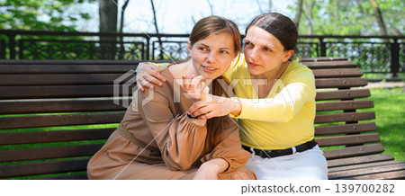 Girls gossiping on a bench in the park 139700282