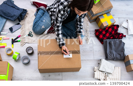 Girl Packs Cardboard Boxes And Takes Photos While Writing The Address On A Box Girl Packs Cardboard Boxes And Takes Photos While Writing The Address On A Box 139700424