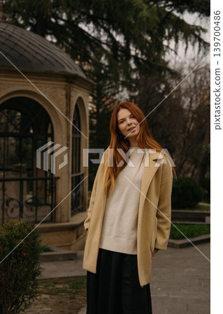 red-haired girl stands outdoors near a building in a park during daylight in a city setting red-haired girl stands outdoors near a building in a park during daylight in a city setting 139700486