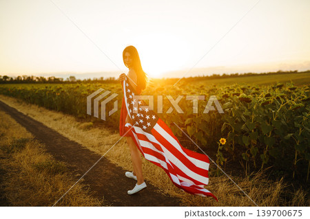 Beautiful girl in hat with the American flag in a sunflower field. 4th of July. Fourth of July. Independence Day. Beautiful girl in hat with the American flag in a sunflower field. 4th of July. Fourth of July. Independence Day. 139700675