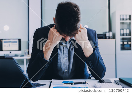 Tired worker. A tired businessman works in the evening. A man in office clothes is holding his temples. Problems in business. The businessman is trying to solve the problems that have arisen. 139700742