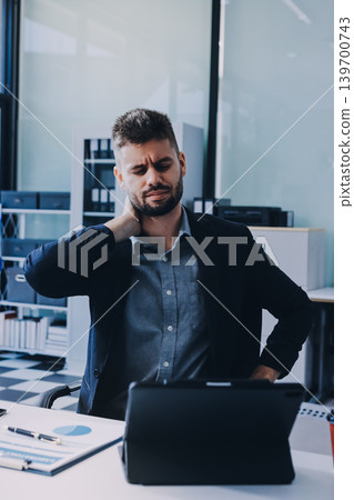 Tired worker. A tired businessman works in the evening. A man in office clothes is holding his temples. Problems in business. The businessman is trying to solve the problems that have arisen. 139700743