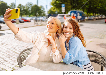 Beautiful woman friends take selfie together, while sitting at outdoor coffee shop. Tourism concept. Beautiful woman friends take selfie together, while sitting at outdoor coffee shop. Tourism concept. 139700811