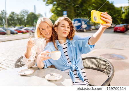 Beautiful woman friends take selfie together, while sitting at outdoor coffee shop. Tourism concept. Beautiful woman friends take selfie together, while sitting at outdoor coffee shop. Tourism concept. 139700814