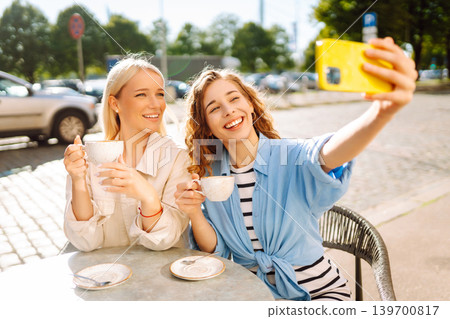 Beautiful woman friends take selfie together, while sitting at outdoor coffee shop. Tourism concept. Beautiful woman friends take selfie together, while sitting at outdoor coffee shop. Tourism concept. 139700817