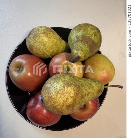 Fresh apples and pears in a black bowl placed on a light surface at a home kitchen setting Fresh apples and pears in a black bowl placed on a light surface at a home kitchen setting 139701021