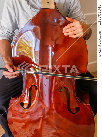 Bass player trying to play broken stringless contrabass. Paradox, persistence, and an impossible effort in hope to make a damaged instrument sound. 139701346