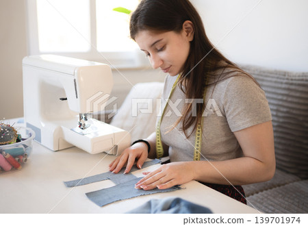 Young girl sewing a piece of fabric at home in the daytime With The sewing machine Young girl sewing a piece of fabric at home in the daytime With The sewing machine 139701974