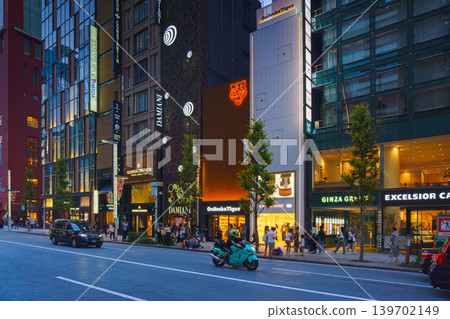 Tokyo, Japan - Oct 14 2024, panoramic view of main street of Ginza district, tall glass facades of skyscrapers along which people walk, cars drive along road, in evening with illumination, Tokyo Japan Tokyo, Japan - Oct 14 2024, panoramic view of main street of Ginza district, tall glass facades of skyscrapers along which people walk, cars drive along road, in evening with illumination, Tokyo Japan 139702149