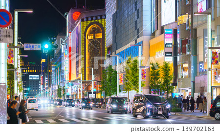 Tokyo, Japan - Oct 14 2024, panoramic view of main street of Ginza district, tall glass facades of skyscrapers along which people walk, cars drive along road, in evening with illumination, Tokyo Japan 139702163