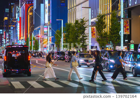 Tokyo, Japan - Oct 14 2024, panoramic view of people crossing road at pedestrian crossing in Ginza district, with many illuminated signage on facades of skyscrapers in background and cars Tokyo, Japan - Oct 14 2024, panoramic view of people crossing road at pedestrian crossing in Ginza district, with many illuminated signage on facades of skyscrapers in background and cars 139702164